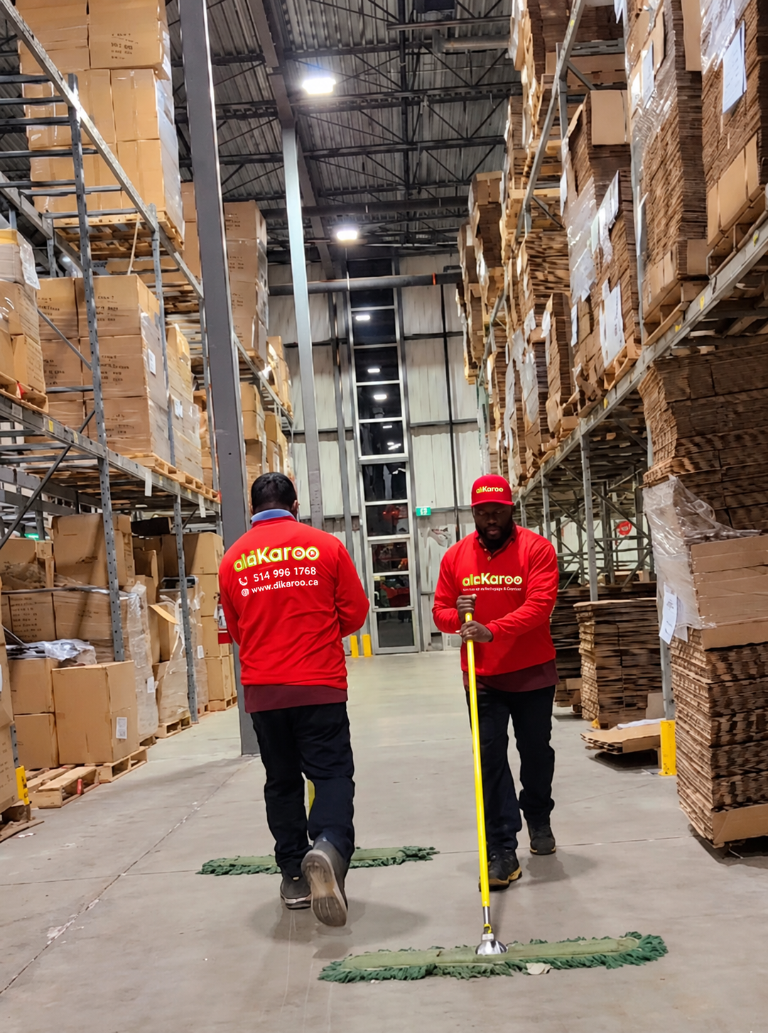 Deux préposés DIKAROO en uniforme rouge lavent le plancher d'une allée d'entrepôt.